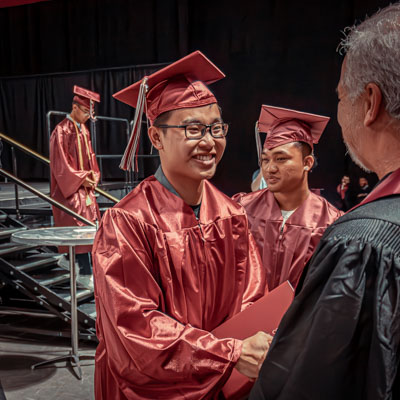 RTC student in graduation regalia, smiling shaking hands with someone