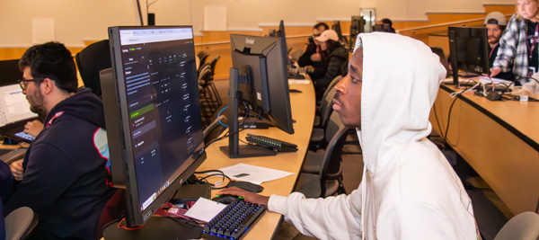 A student in a white hoodie looking at a computer screen in a classroom