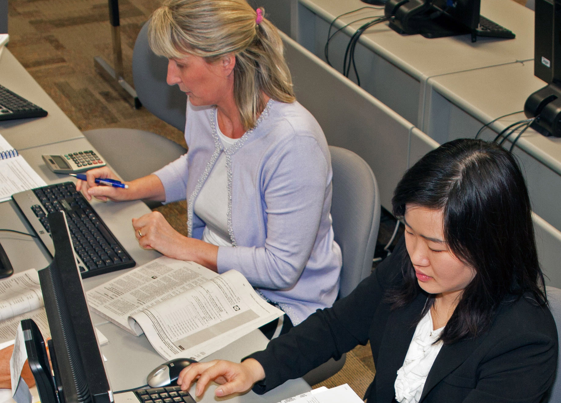 Two people working at computers with textbooks in front of them.