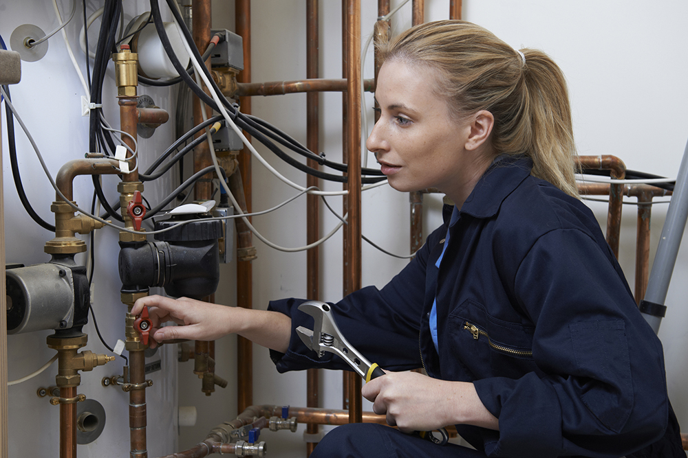 A woman with a wrench repairing a water line.