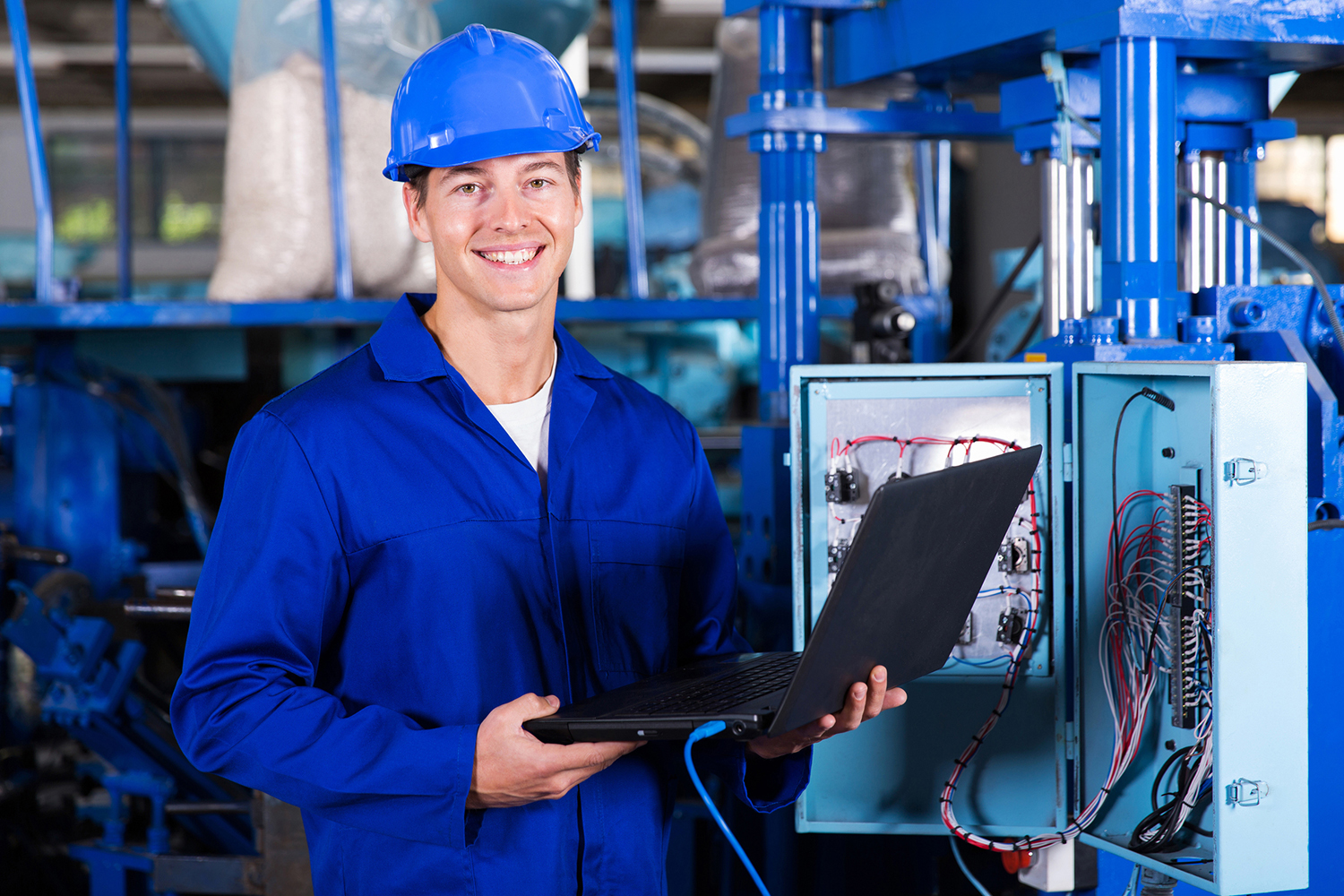 A man holding a laptop in front of an electrical panel.