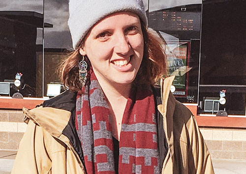 Ali Cohen in a brown coat and striped red and gray scarf, and a gray beanie hat