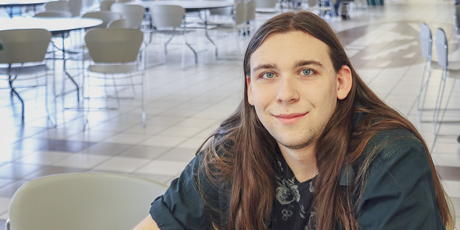 Visiting student smiles at the camera, sitting in the cafeteria